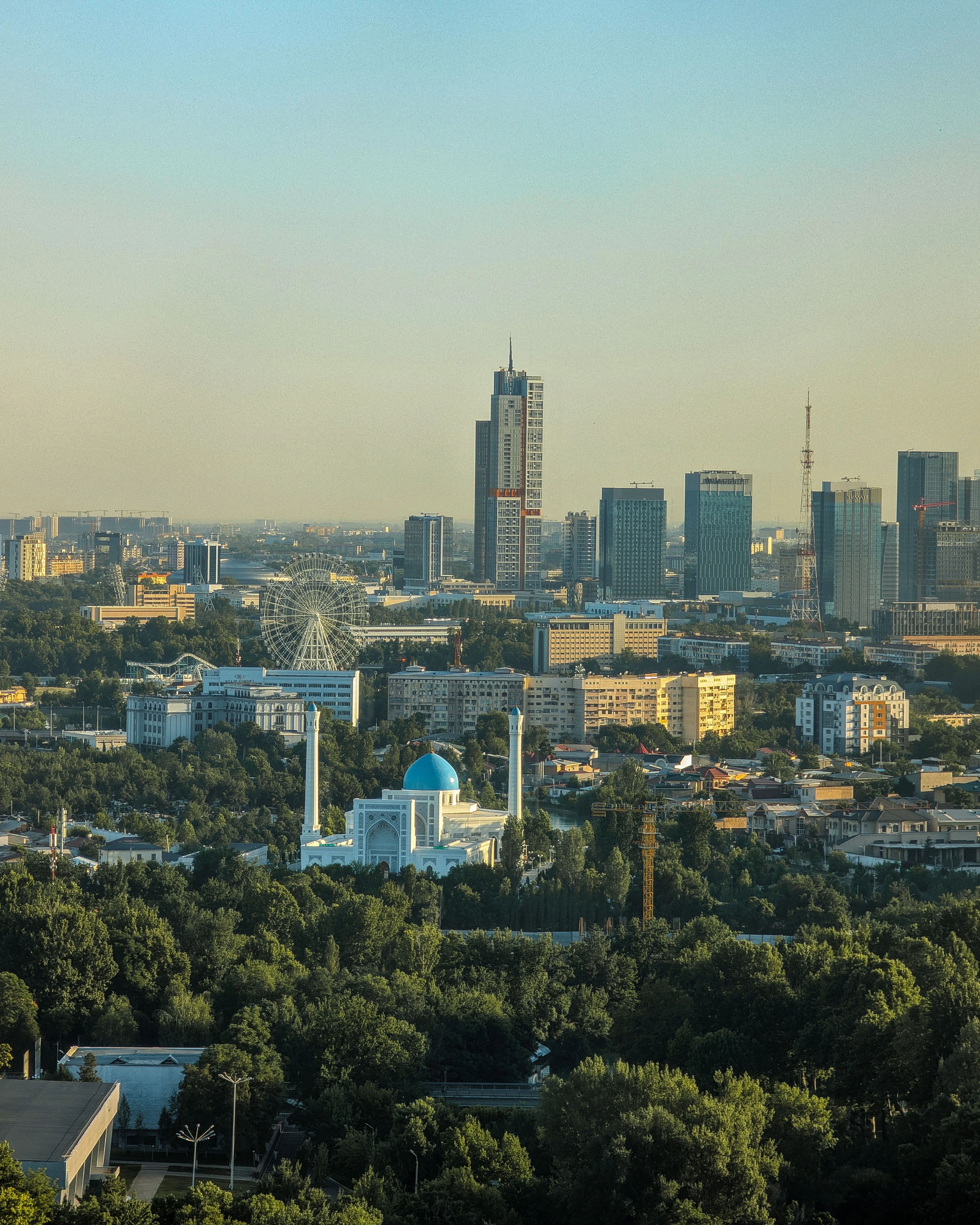 The skyline of Tashkent at sunset, with a blue-domed mosque in the foreground